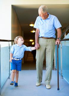 Elderly man with cane walks down hallway with child